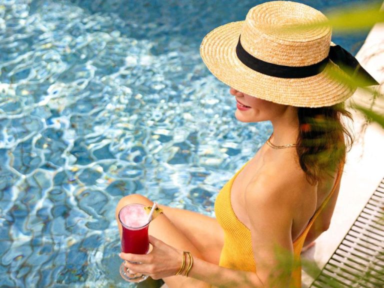 Mujer disfrutando de un cocktail junto a la piscina exterior del Fairmont Singapore en verano