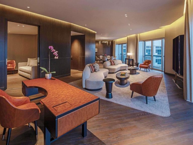 Lujosa suite del Fairmont Singapore con salón amplio, escritorio de cuero y decoración elegante en tonos cálidos