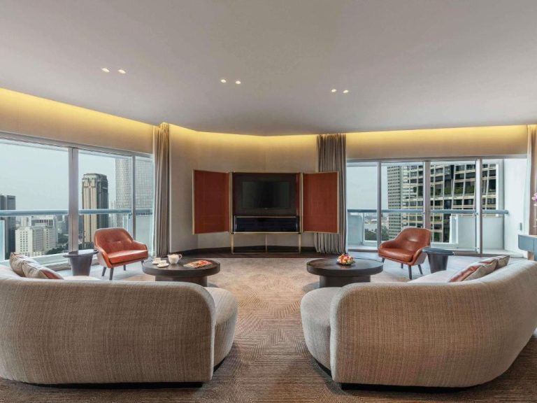 Amplio salón de suite de lujo con sofás, sillones de cuero y vistas panorámicas a Singapur en Fairmont Singapore