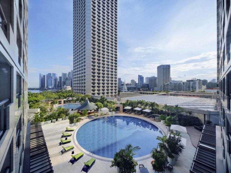 Piscina circular exterior del Fairmont Singapore con tumbonas verdes y vistas al skyline de Singapur