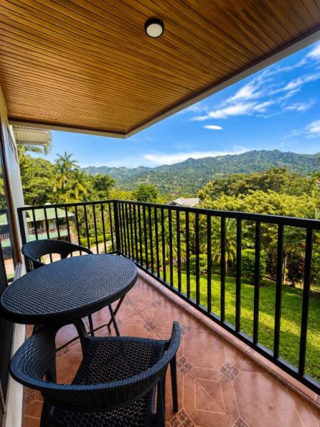 Balcón con mesa y sillas de ratán con vistas a la montaña verde en Hotel Villas de la Colina