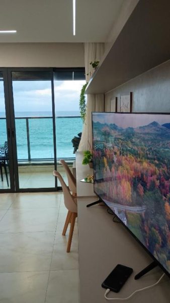 Salón con televisor grande y vistas panorámicas al mar desde el Studio Luxuoso frente Mar