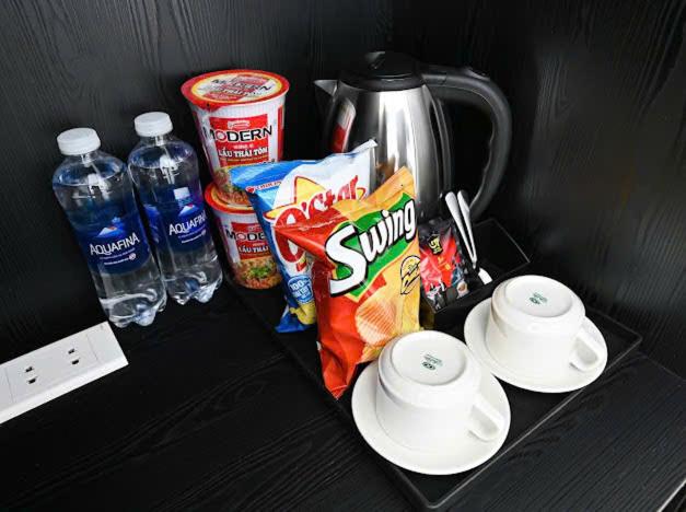 Amenidades de habitación en Victory Hotel Saigon South con hervidor, snacks, tazas y agua Aquafina