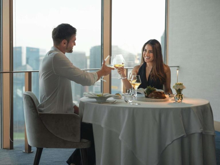 Pareja brindando con vino blanco en cena romántica con vistas a Singapur en Swissotel The Stamford