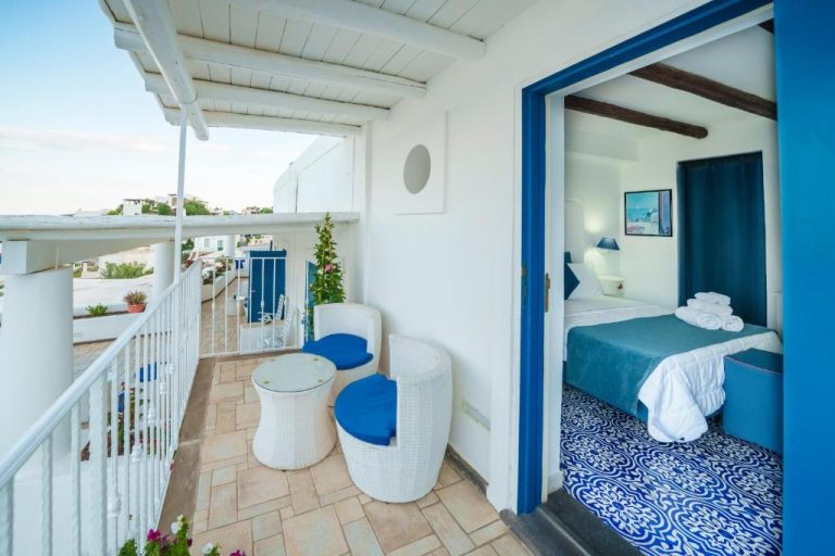 Terraza con sillas y mesa del Hotel La Terrazza con acceso a habitación doble de decoración azul y blanca