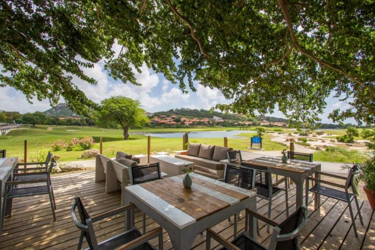 Terraza exterior con mesas de madera y vistas al campo de golf en Blue Bay Lodges Curazao